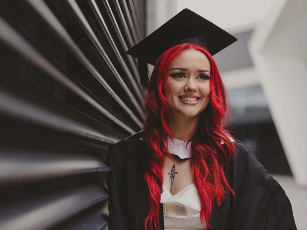 An RGU student with red hair wearing a graduation cap and gown