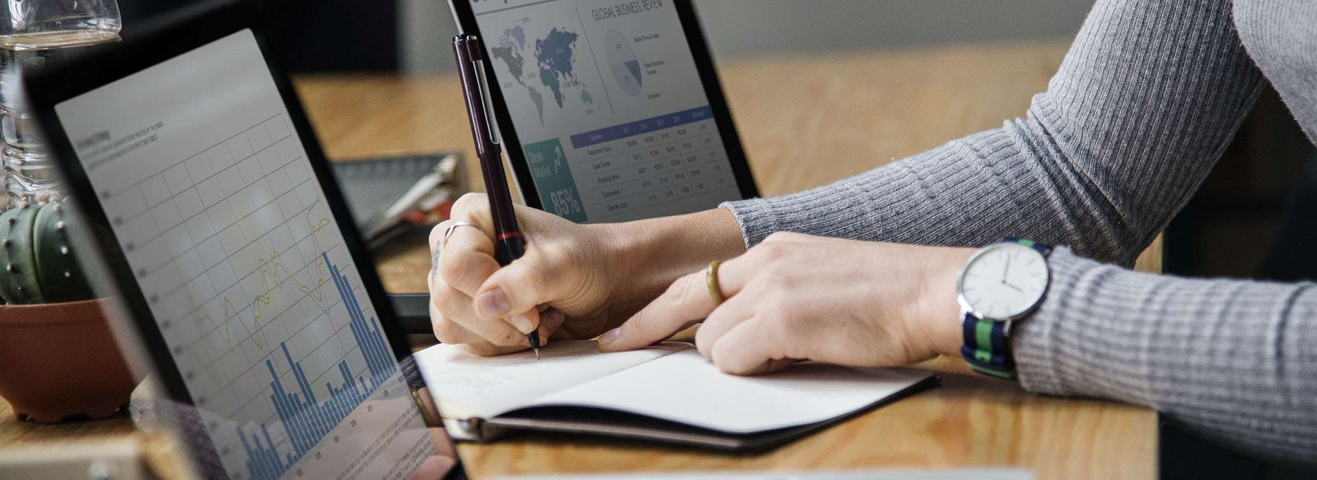 someone taking notes next to screens with graphs