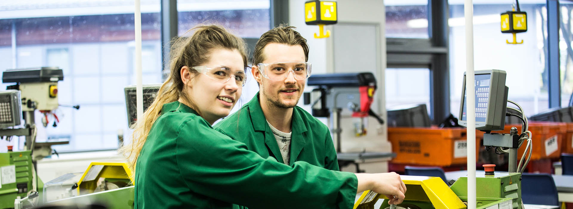 two students in engineering overalls at machines