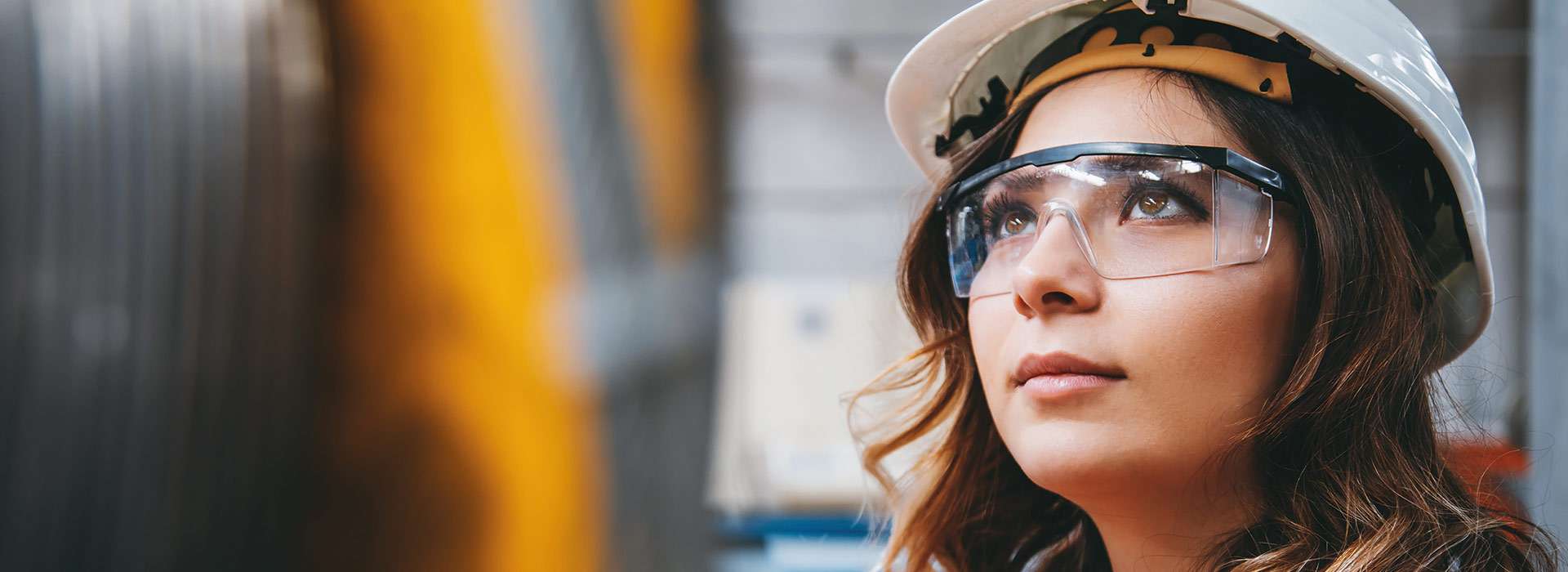 woman in hard hat and safety glasses looking up