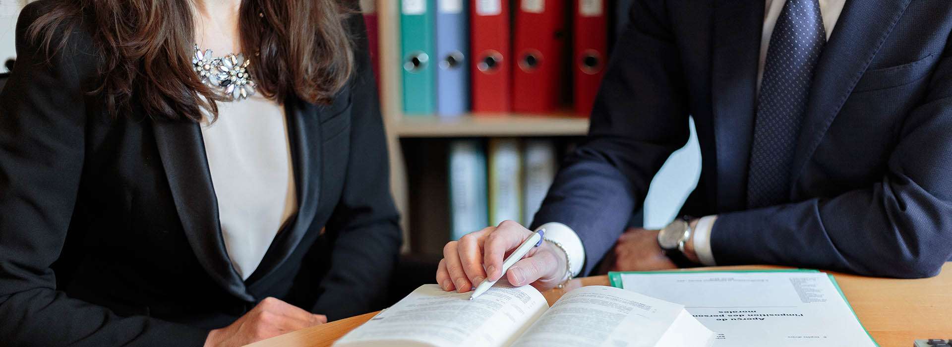 two professional people pointing at a book with a pen