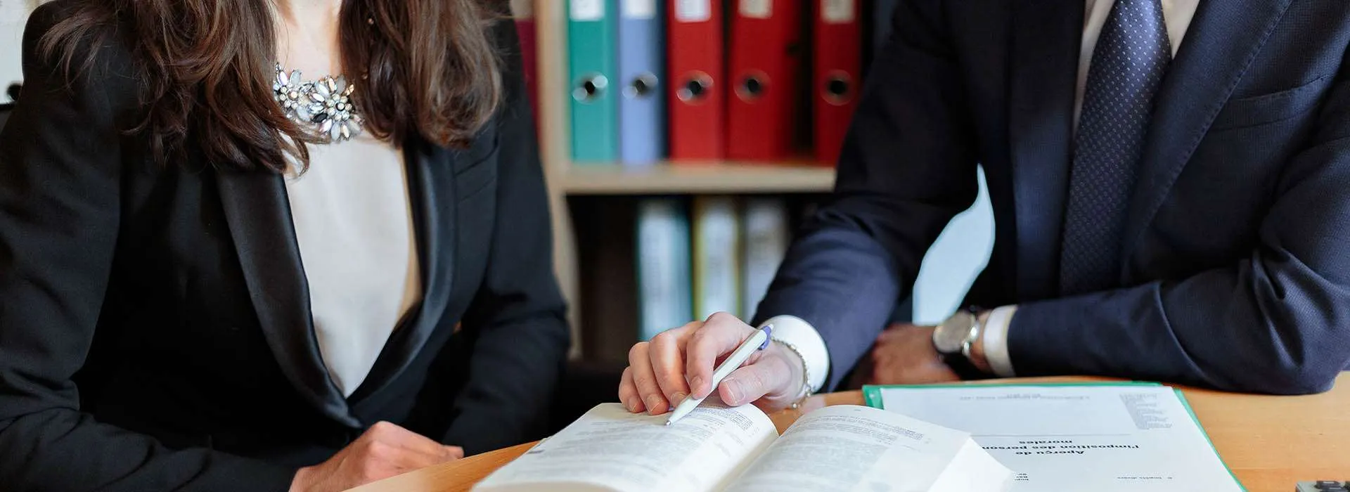 two professional people pointing at a book with a pen