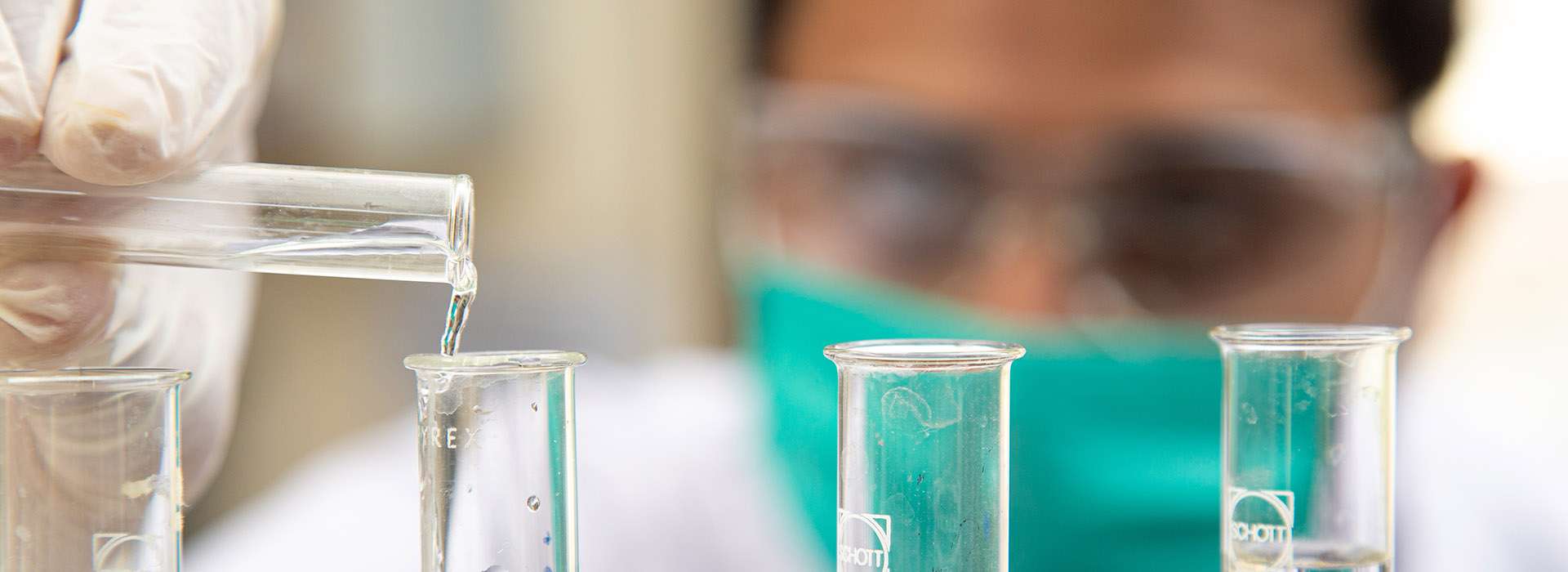 man in mask using pippettes and test tubes