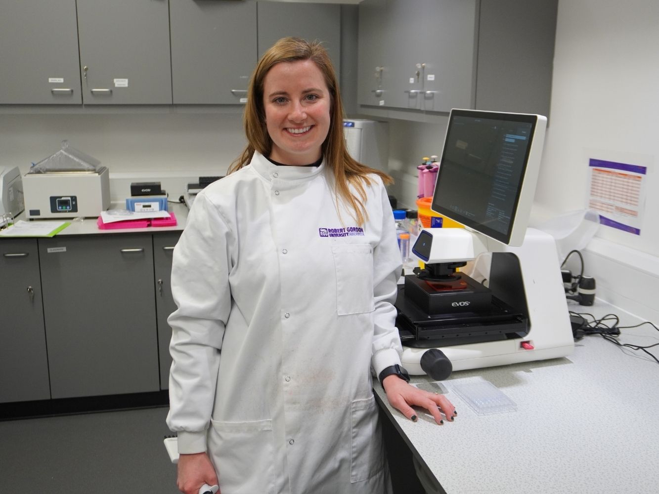 Dr Gael Morrow wearing a white coat in a lab
