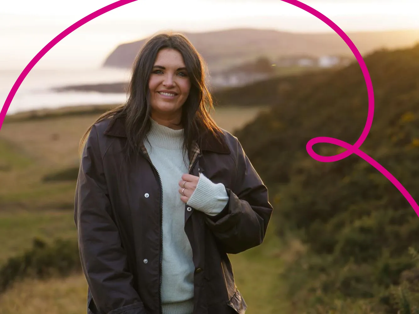 Julia Bryce smiles towards the camera with coastal countryside scenes in the background