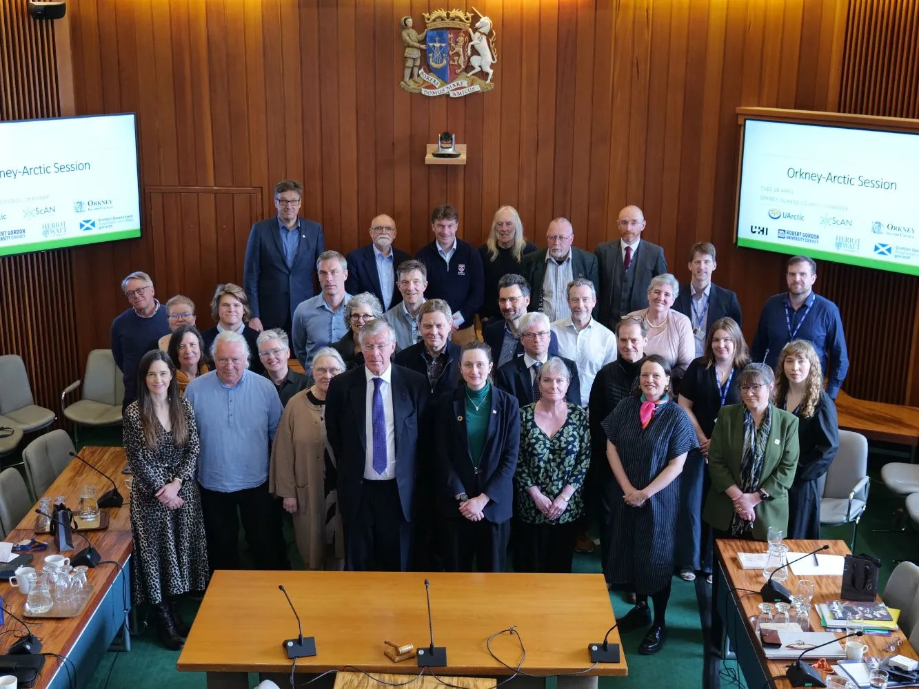 A group of people posing with a wood panel wall and Orkney Islands Council symbol behind them