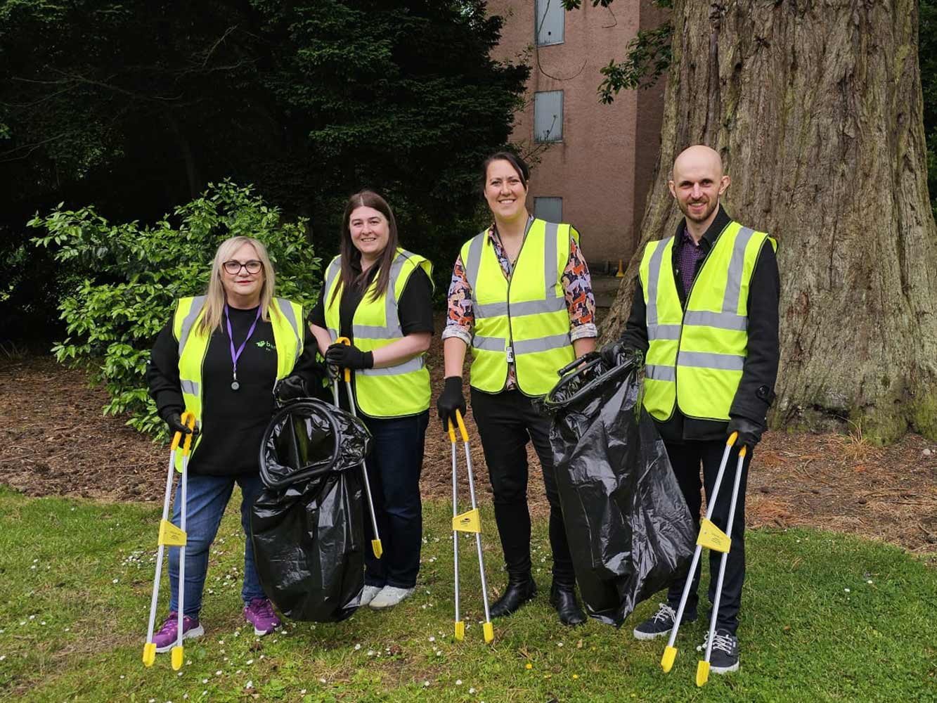 4 people standing outside wearing high viz with rubbish bags and litter pickers