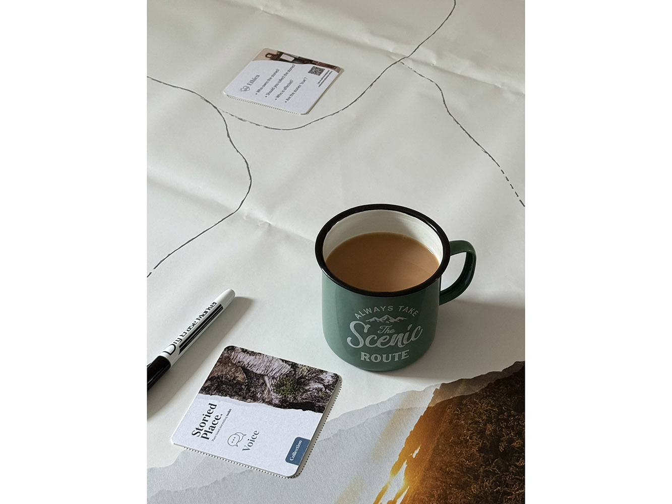 A green cup of tea, a coaster and a pen on a white tablecloth