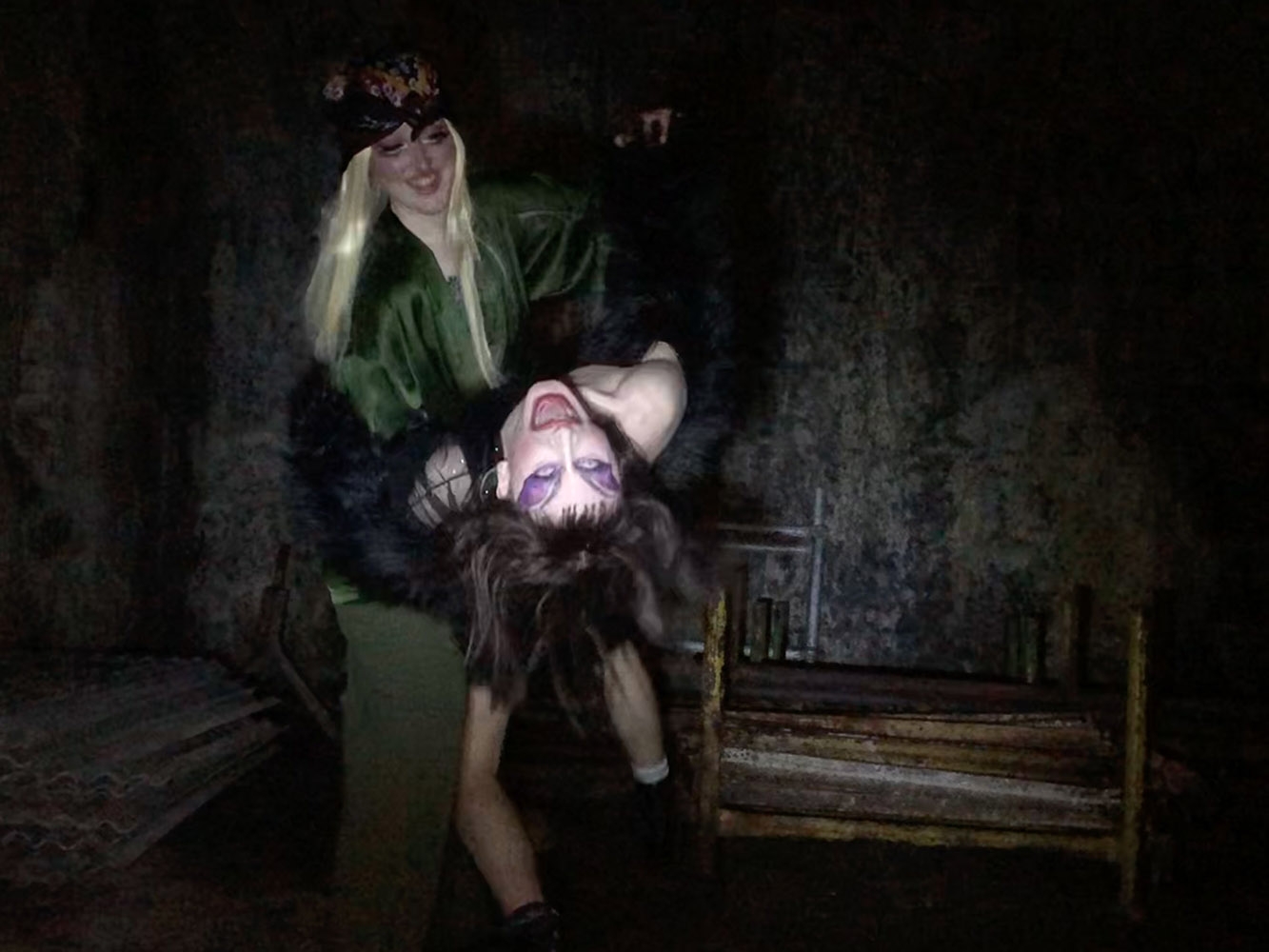 Two drag queens dance in a dark room