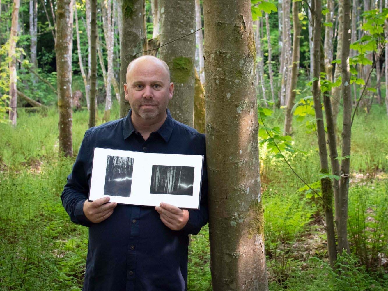 Paul Nichol standing in woodland setting holding book featuring two images