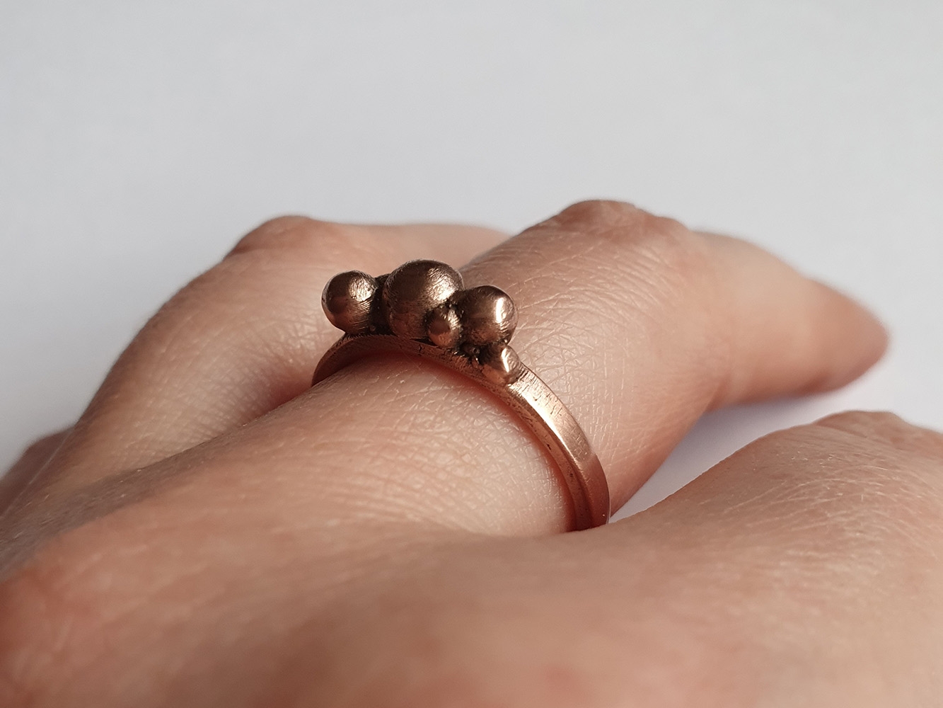 Copper ring with band and multiple spheres on top worn on a hand