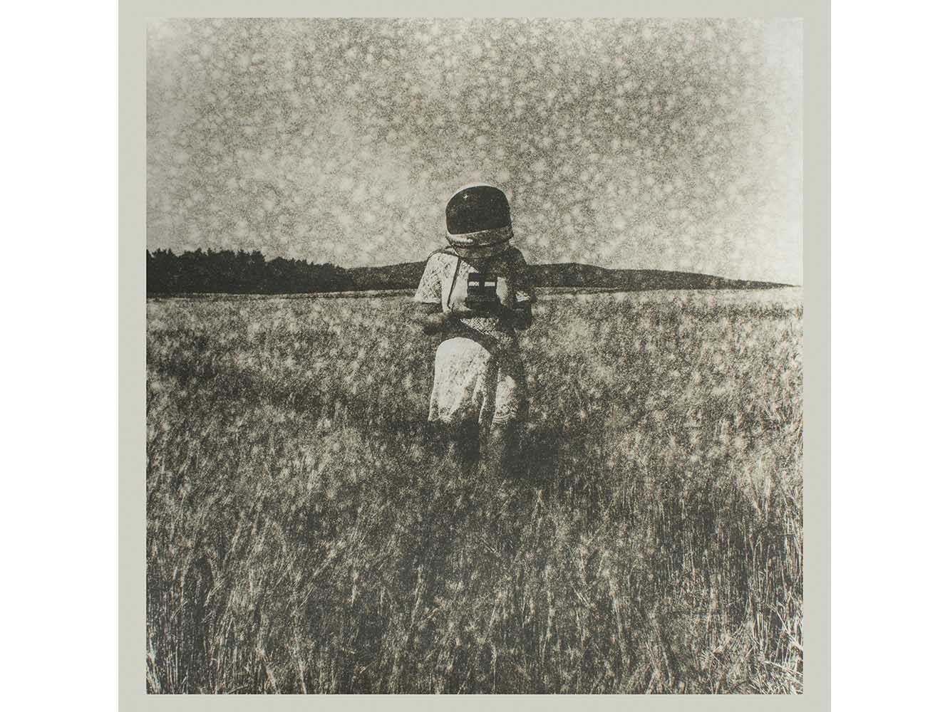 Black and white photograph of person in space helmet in a field