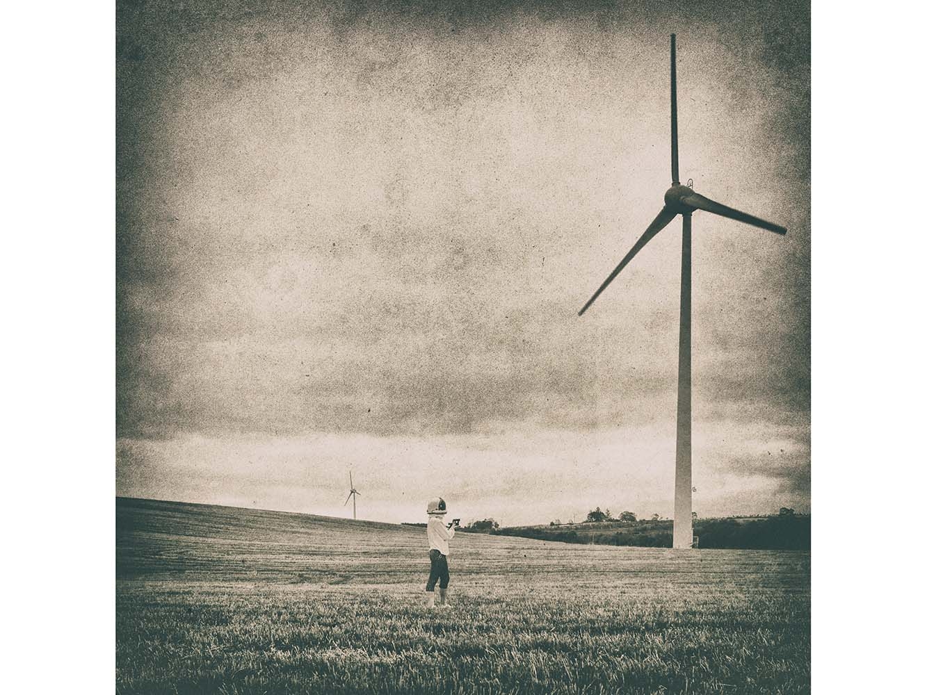 Black and white photograph of person in space helmet looking at a wind turbine