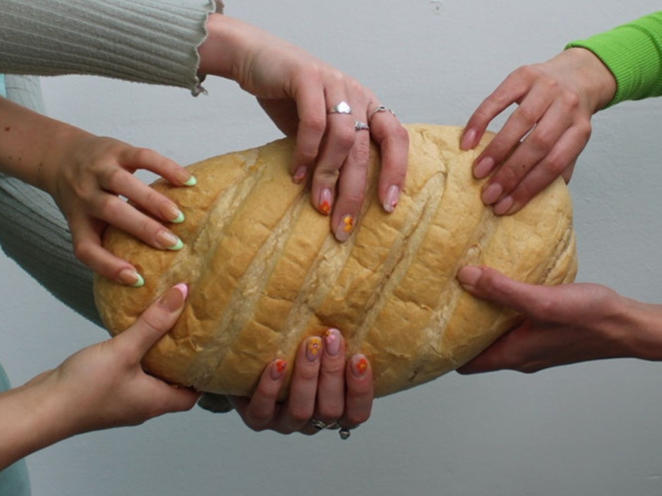 Six hands holding a large loaf of bread