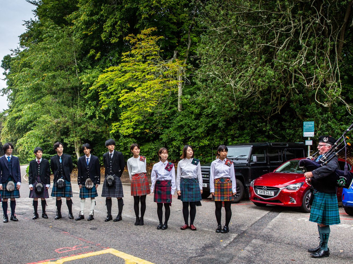 Japanese students in traditional Scottish dress accompanied by a bagpiper
