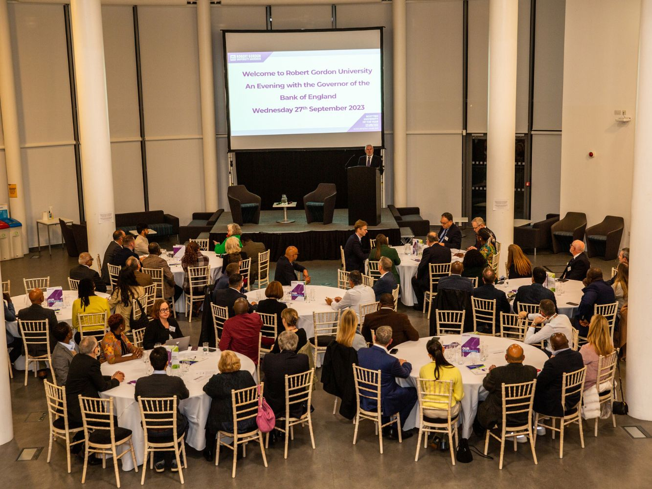 Attendees watch a presentation on round tables in the atrium of the Sir Ian Wood Building.