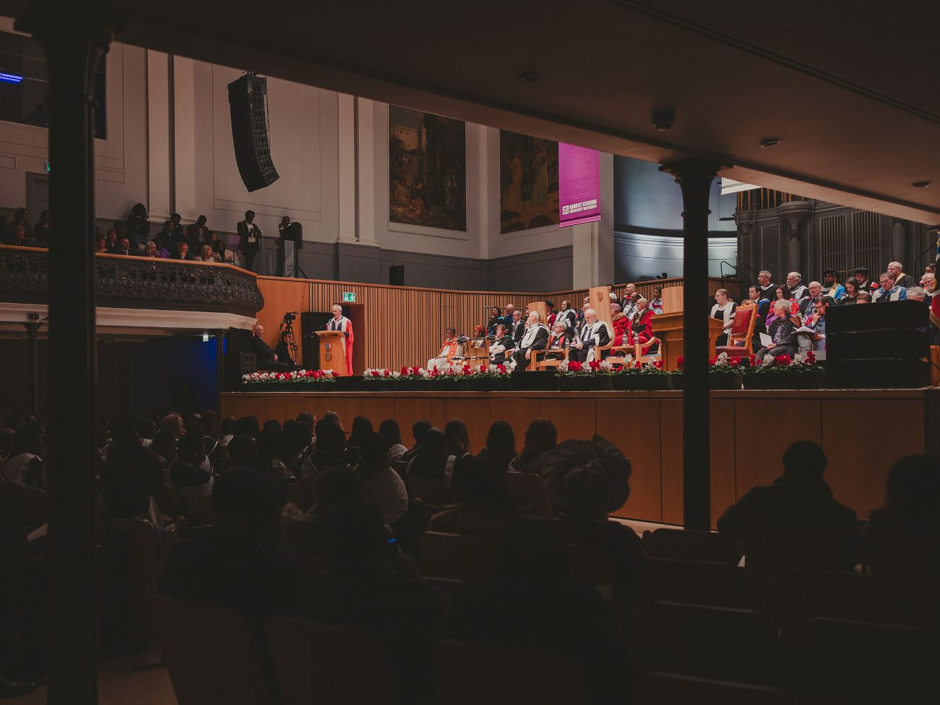 An image taken from the distance looking on the stage as Mark gives his speech in front of a packed Music Hall audience
