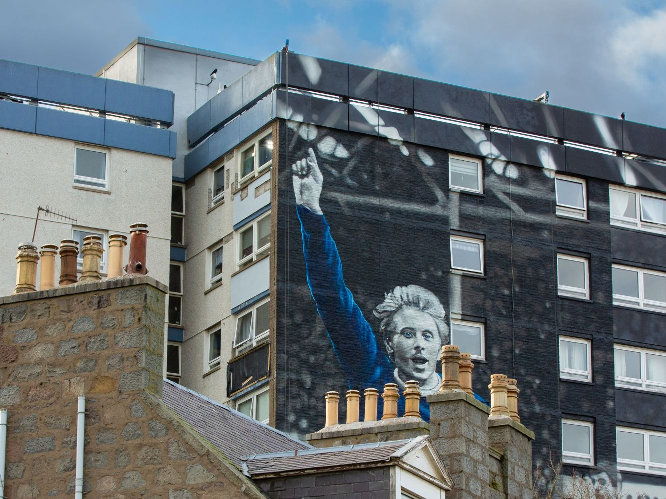 An aerial shot of Denis Law Scotland mural in the background, with chimney pots in the fore