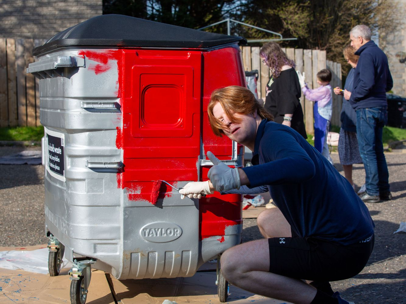 Harvey paints one of the community bins in red, smiling towards the camera