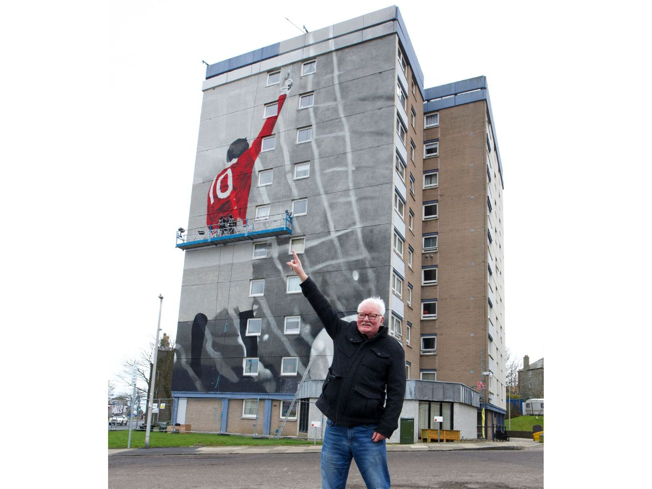 Jim Gray stands pointing backwards towards the mural, which was still being complete