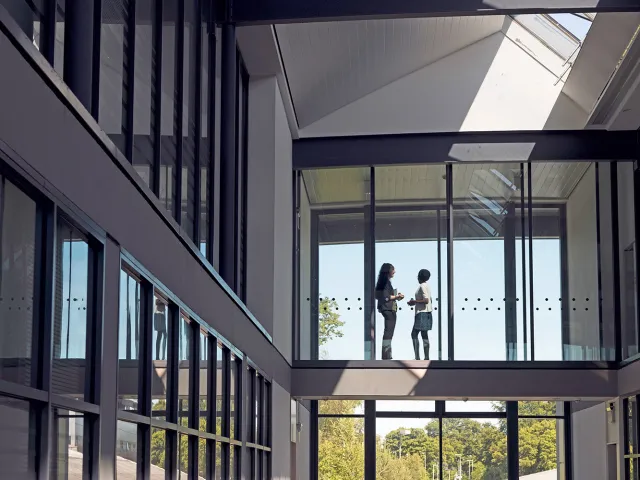 two students chatting on a walkway in front of a window