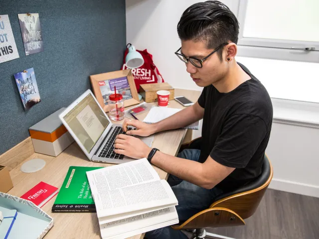 student working at his desk with a book and laptop