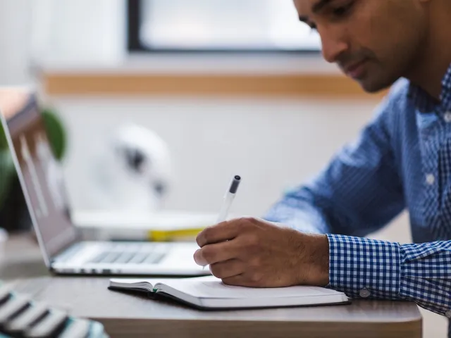 Person writing with a laptop nearby