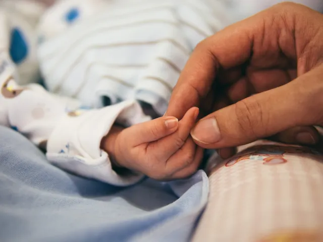 adult hand holding infant hand