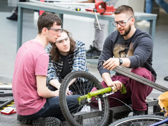 students wearing safety goggles constructing a vehicle with a bicycle wheel