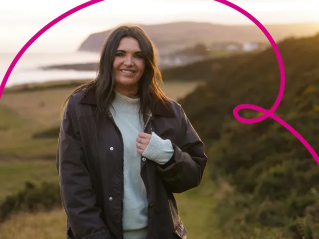 Julia Bryce smiles towards the camera with coastal countryside scenes in the background