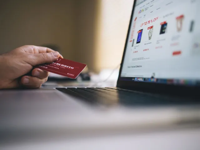 hand holding credit card next to laptop