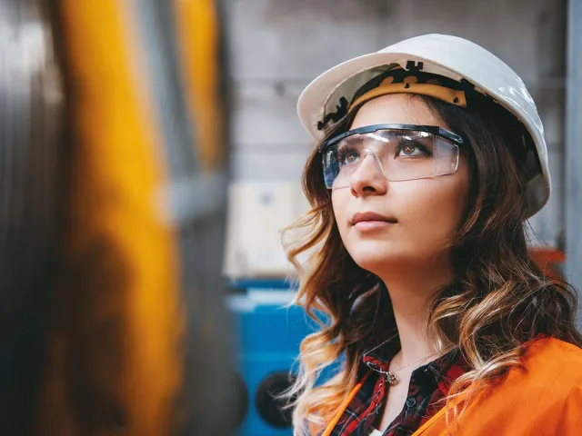woman in hard hat and safety glasses looking up