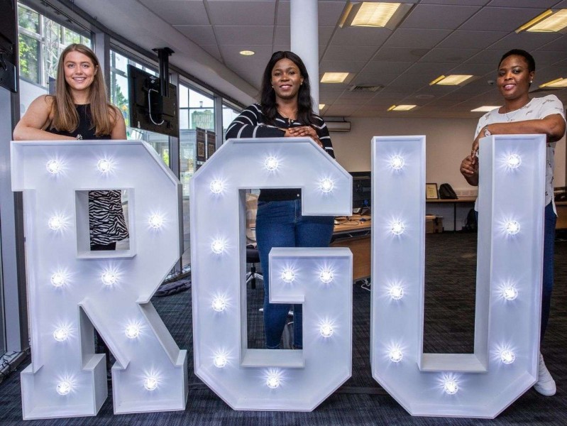 four student presidents lean on RGU light up sign