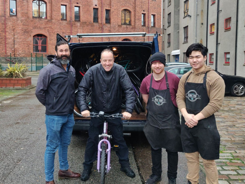 Four people by van filled with bikes, one person sits on bike