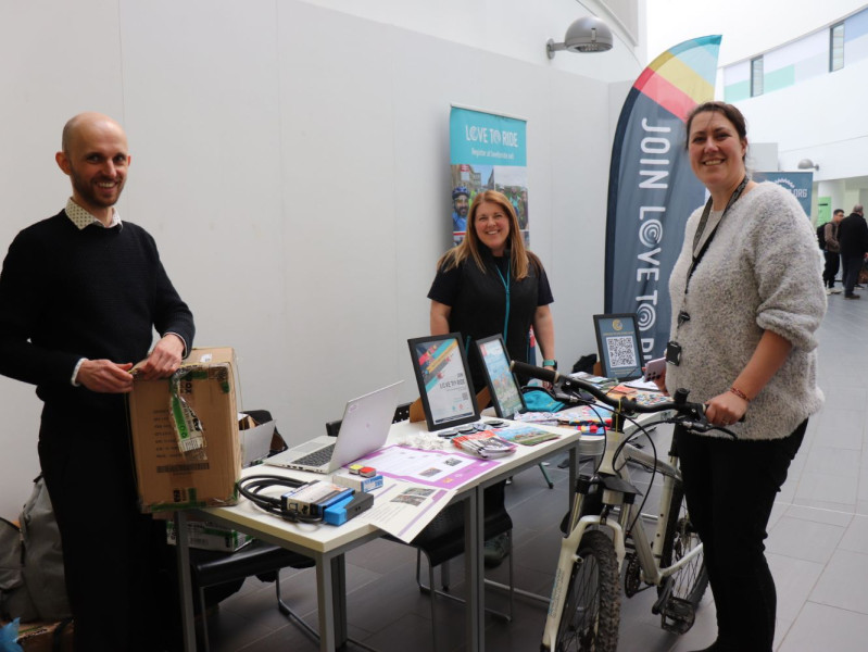 Three RGU staff members at a stall in the Sir Ian Wood Building with one holding a bike
