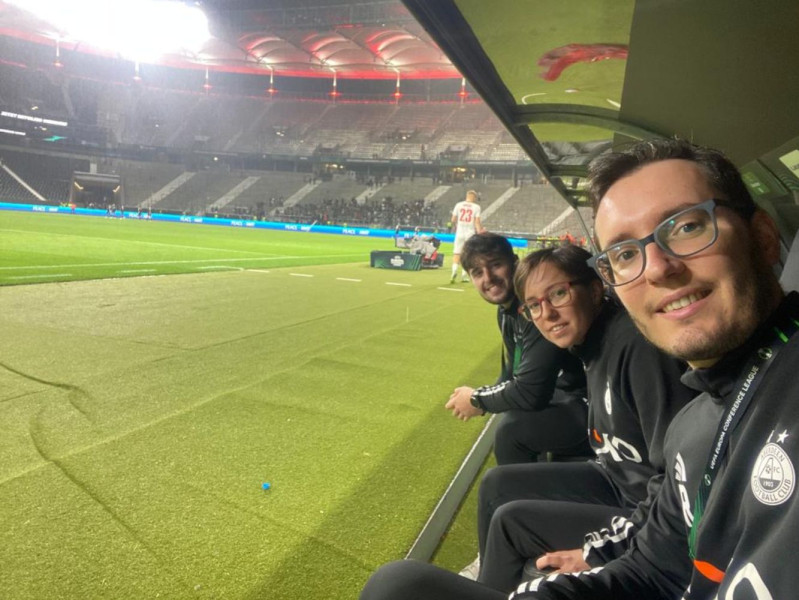 Dylan Banfield with Aberdeen FC's Marti and Jordi Rams sit in a football dugout with the pitch to their left