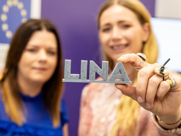 Two women holding up the LINA logo