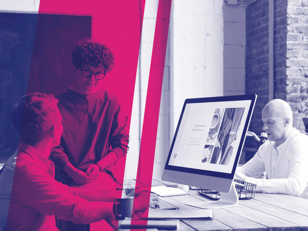 Two people talking in front of a computer in a workspace Two people talking in front of a computer in a workspace