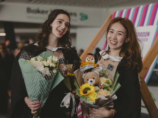two graduates holding flowers two graduates holding flowers