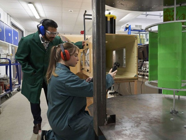 Two people in green overalls looking at engineering equipment