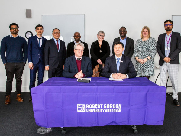 RGU & KBTU members stand and sit at a table