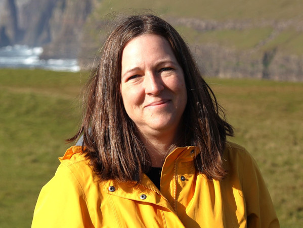 Lisa Luken smiling in a yellow jacket in front of rugged landscape