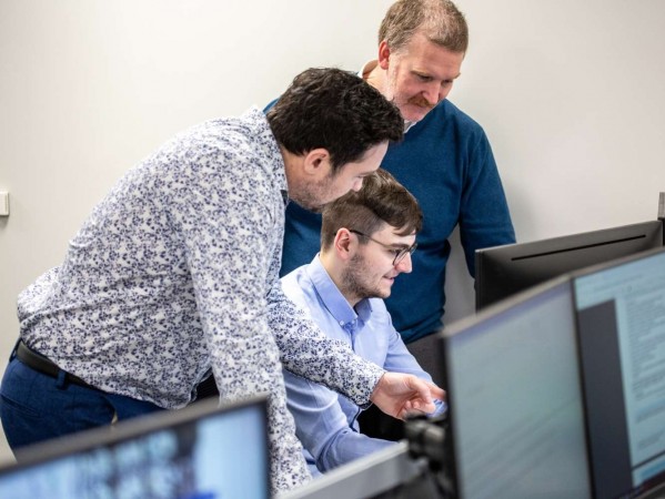 three people in discussion surrounding one computer