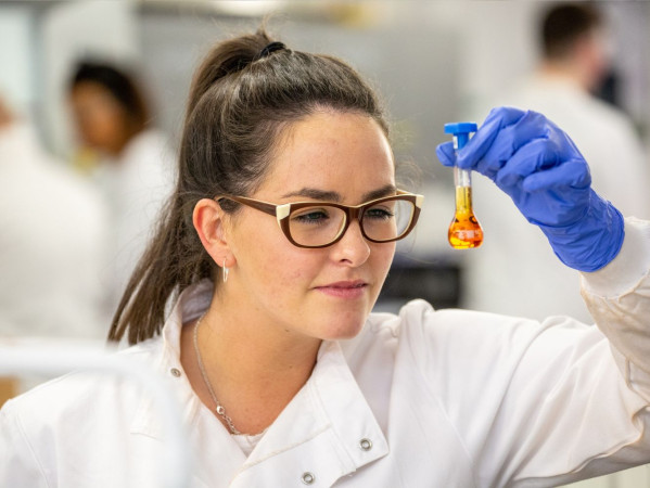 A person wearing a white coat looks at test tube