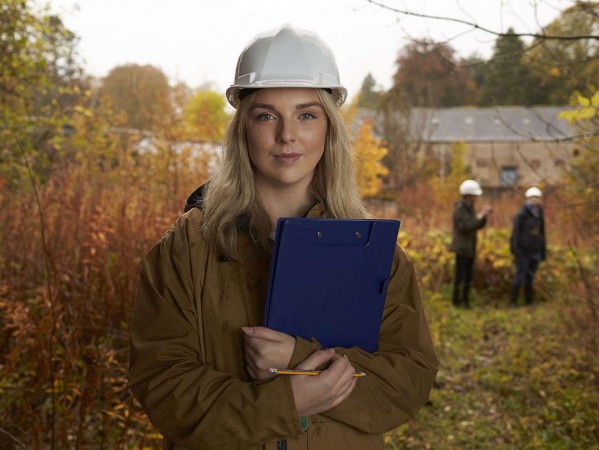 woman in a hard had standing in a field holding a clipboard woman in a hard had standing in a field holding a clipboard