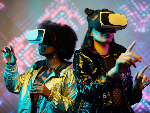 Two people wearing VR headsets with brightly coloured lights behind them