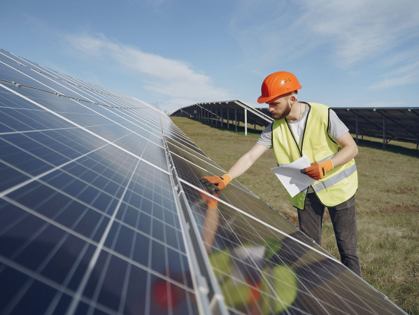 person in hig-viz jacket and hard hat looking at solar panels in a field