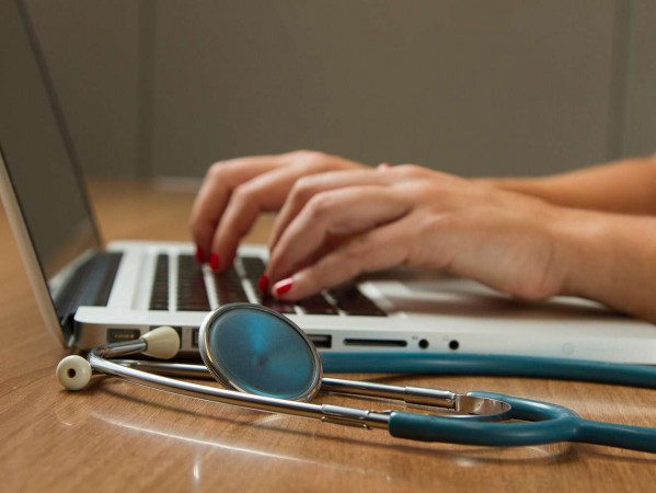 woman typing on a laptop with stethoscope on the desk