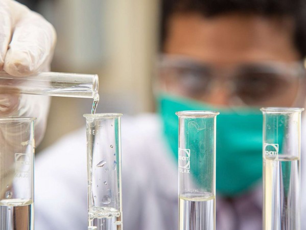 man in mask using pippettes and test tubes